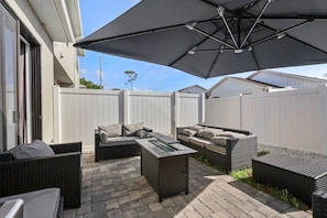 An outdoor patio with wicker furniture, a glass-top table, and a large umbrella providing shade. - Terra Esmeralda Home Near Disney for 9 Guests (Kissimmee)
