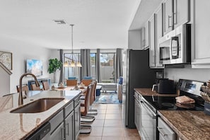 A modern kitchen with granite countertops, stainless steel appliances, and a dining area with a view. - Terra Esmeralda Home Near Disney for 9 Guests (Kissimmee)