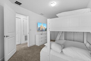 Een slaapkamer met een stapelbed, witte muren, een deur, een dressoir en een schilderij.