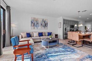 A modern living room with a sofa, coffee table, and chairs. There is a kitchen area with a dining table and chairs. - Terra Esmeralda Home Near Disney for 9 Guests (Kissimmee)