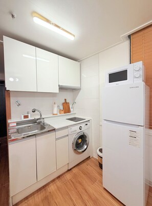 A compact kitchen with white cabinets, a stainless steel sink, a built-in washing machine, and a Samsung refrigerator. - Stay in Trendy Yongsan /Seoul /3-min walk to Subway & Airport Bus (Seoul)