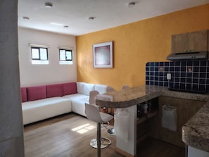 A modern kitchen with a built-in island, a white sofa with red cushions, and a blue tiled backsplash. - A minimalist and functional loft in the Mexican style, located in the heart of Coyoacán (Ciudad de México)