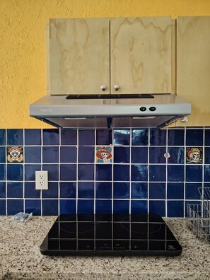 A kitchen with a black induction cooktop, a stainless steel range hood, and a backsplash with blue tiles featuring decorative skull motifs. - A minimalist and functional Mexican-style loft in the heart of Coyoacán (Ciudad de México)