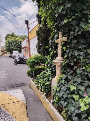 A street with a white building, a stone cross, and a motorcycle parked on the side. - A minimalist and functional Mexican-style loft in the heart of Coyoacán (Ciudad de México)