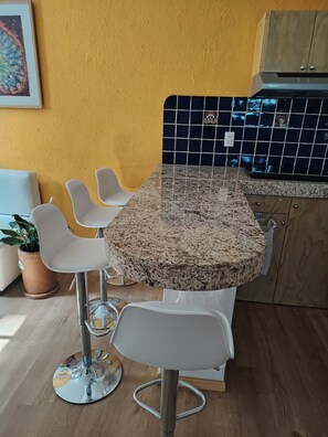 A kitchen with a granite countertop, white chairs, a potted plant, and a yellow wall. - A minimalist and functional loft in the Mexican style, located in the heart of Coyoac án (Ciudad de México)