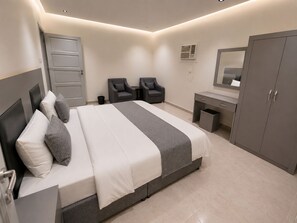 A modern bedroom with a large bed, two chairs, a desk, and a wardrobe. - Luxury Modern Apartment  Near Alharam  And Airport (Madinah)