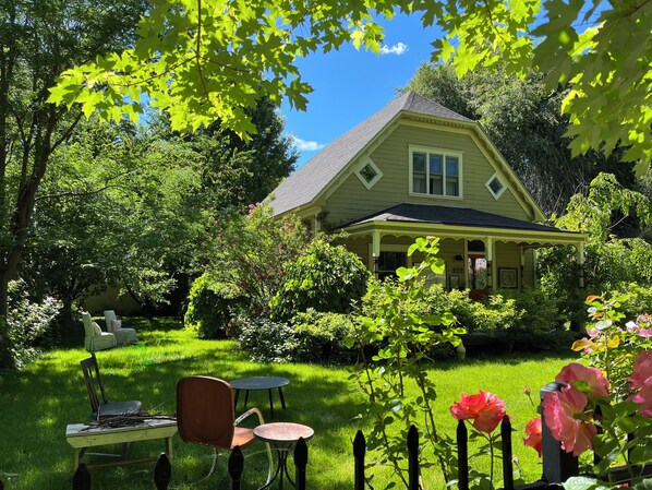 Ett hus med en inglasad veranda, omgivet av en välskött trädgård med olika växter och blommor.