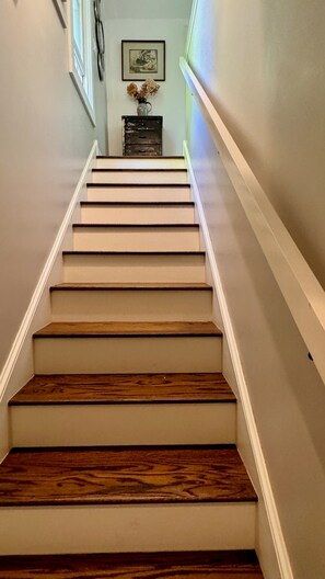 Eine Treppe mit Holzbodenstufen und weißen Wänden, die zu einer Empore mit einer Vase getrockneter Blumen führt.