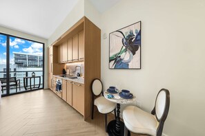 A modern kitchen with wooden cabinets, a marble countertop, and a dining area with two chairs and a table. - High Floor Wynwood Studio - Rooftop Pool & Spa (Miami)