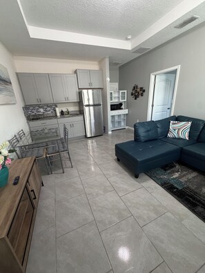 A modern kitchen with grey cabinets, a stainless steel refrigerator, and a dining area with a glass table and chairs. - Cozy 1-bedroom apartment in Kissimmee (Kissimmee)