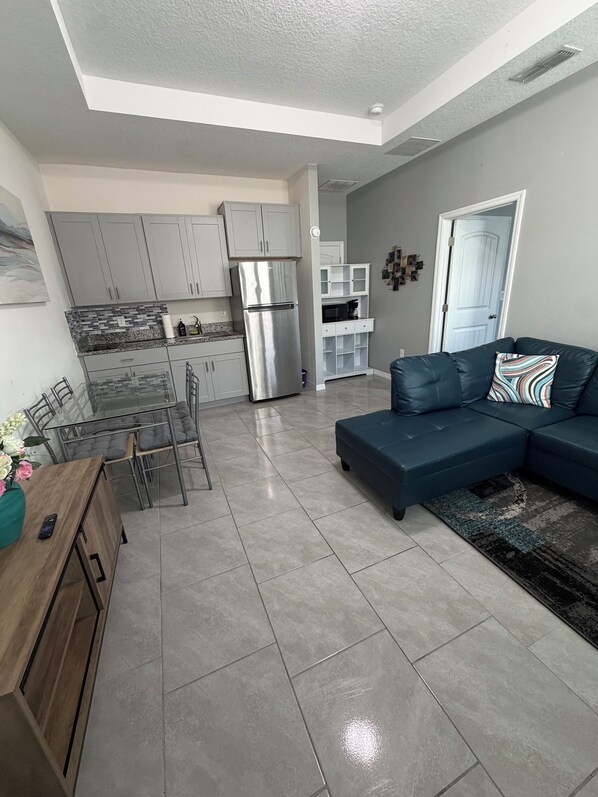 A modern kitchen with grey cabinets, a stainless steel refrigerator, and a dining area with a glass table and chairs.