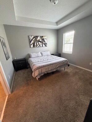 A bedroom with a bed, a nightstand, a wall-mounted artwork, and a window. - Cozy 1-bedroom apartment in Kissimmee (Kissimmee)