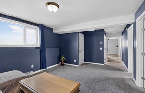 A hallway with a carpeted floor, a wooden bench, a potted plant, and a door at the end.