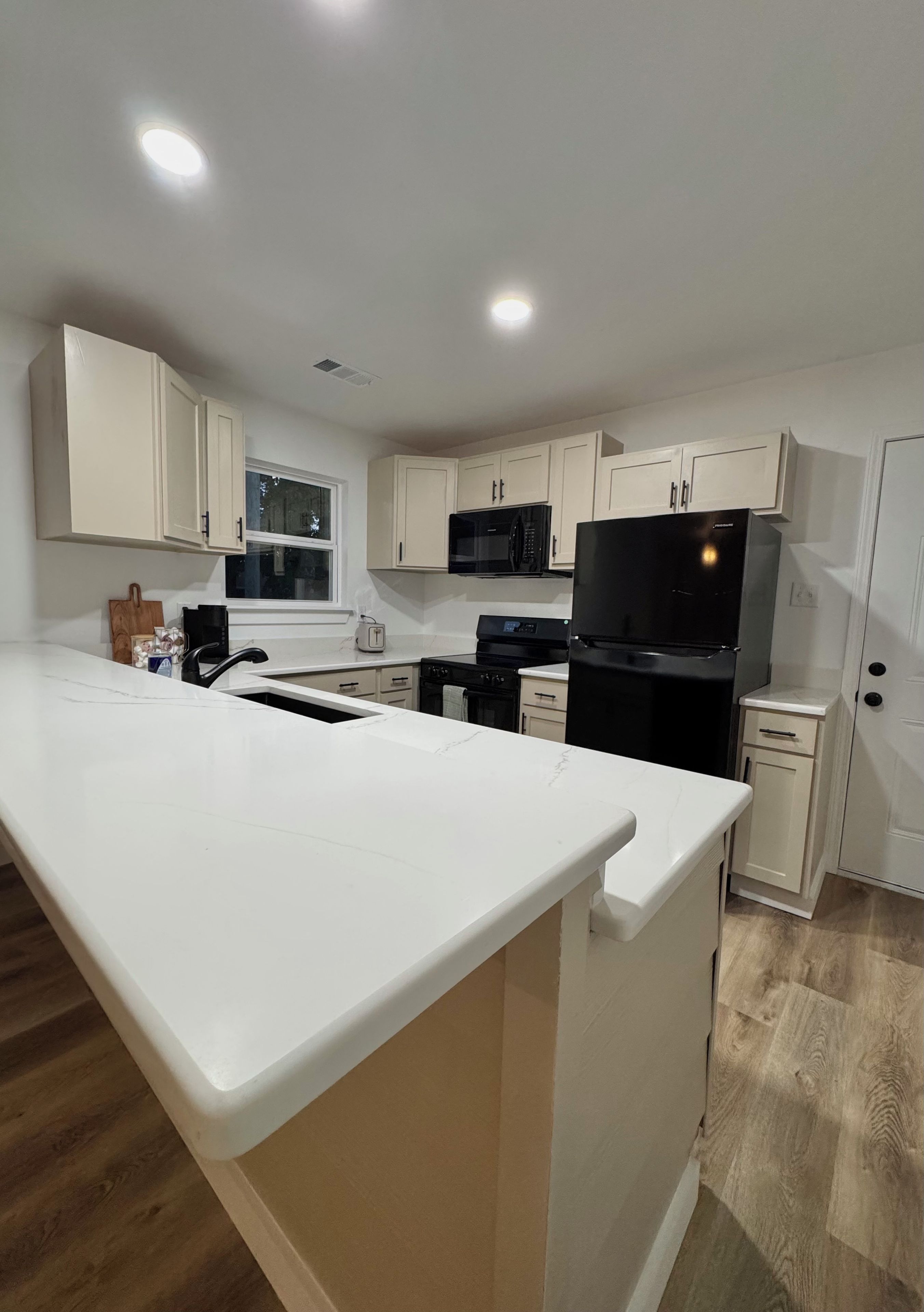 A modern kitchen with white cabinetry, a black refrigerator, and a large island.