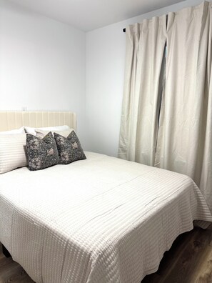 A bed with a quilted white cover, two patterned pillows, a headboard, and a window with curtains. - Fantastic 3-bedroom house in vibrant Jacksonville (Jacksonville)