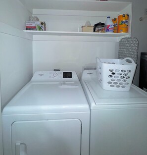 A front-loading Whirlpool washer and dryer stacked in a laundry room with a shelf above containing cleaning supplies. - Fantastic 3-bedroom house in vibrant Jacksonville (Jacksonville)