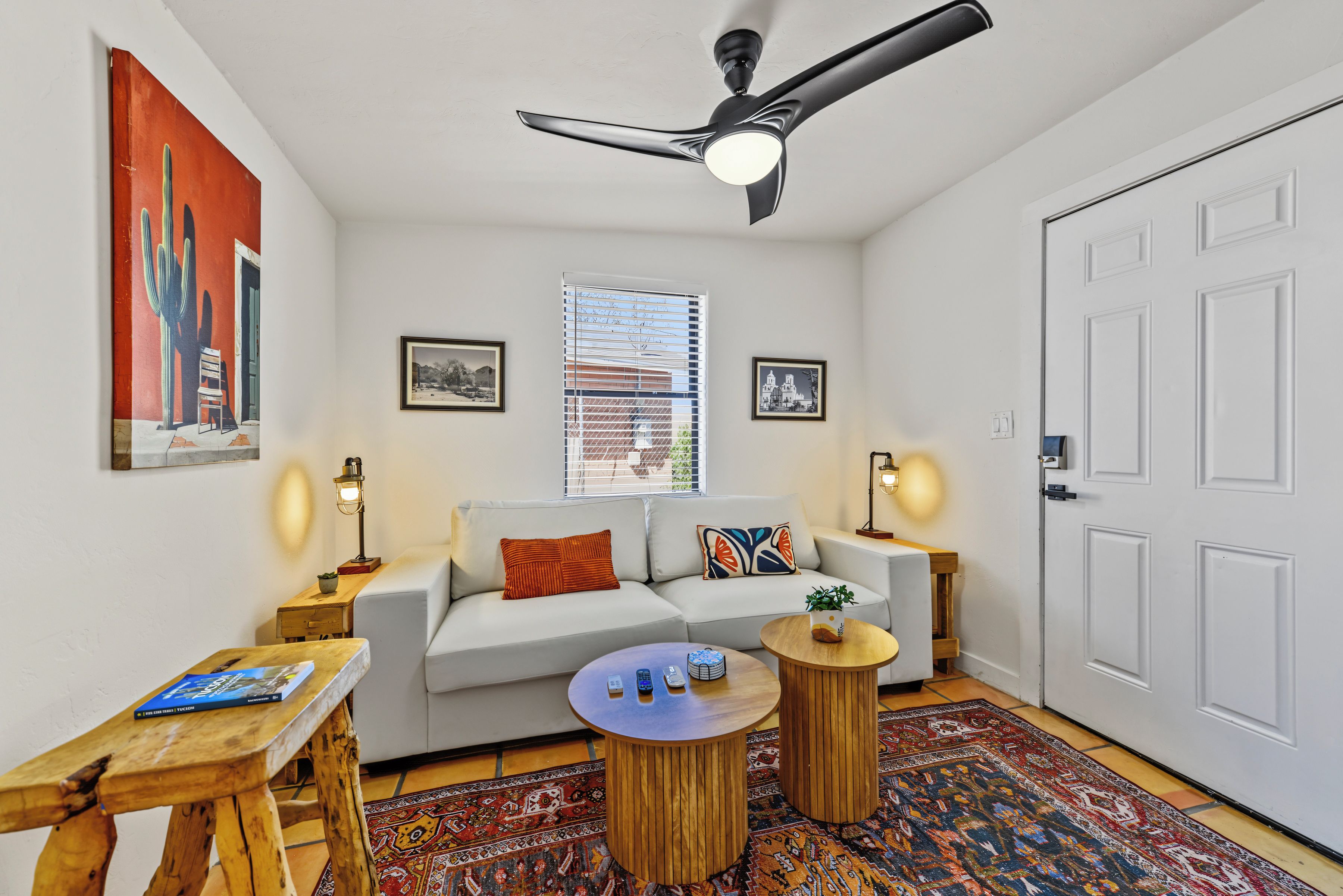 A modern living room with a sofa, two side tables, a ceiling fan, and a window with blinds.