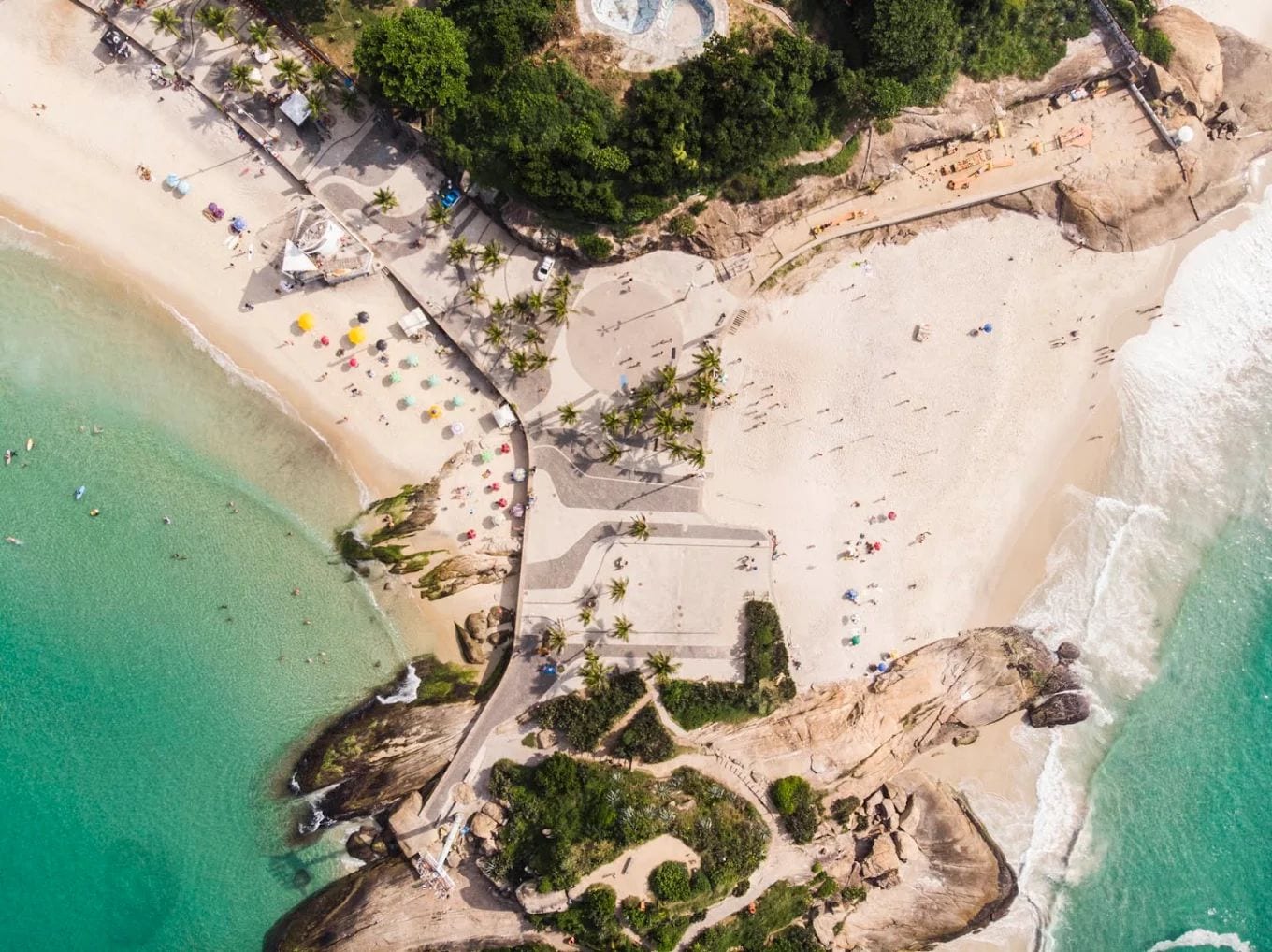 Vue aérienne d’une plage aux eaux turquoise et limpides, bordée d’un rivage sablonneux et ponctuée de quelques parasols.