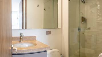 Un bagno con cabina doccia in vetro, un water bianco e un lavabo con piano di appoggio color beige.