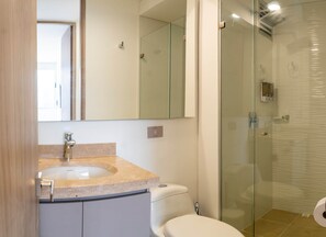 A bathroom with a glass shower enclosure, a white toilet, and a sink with a beige countertop. - Sereno Stays · 3BR Apartment, Santa Marta (Unknown)