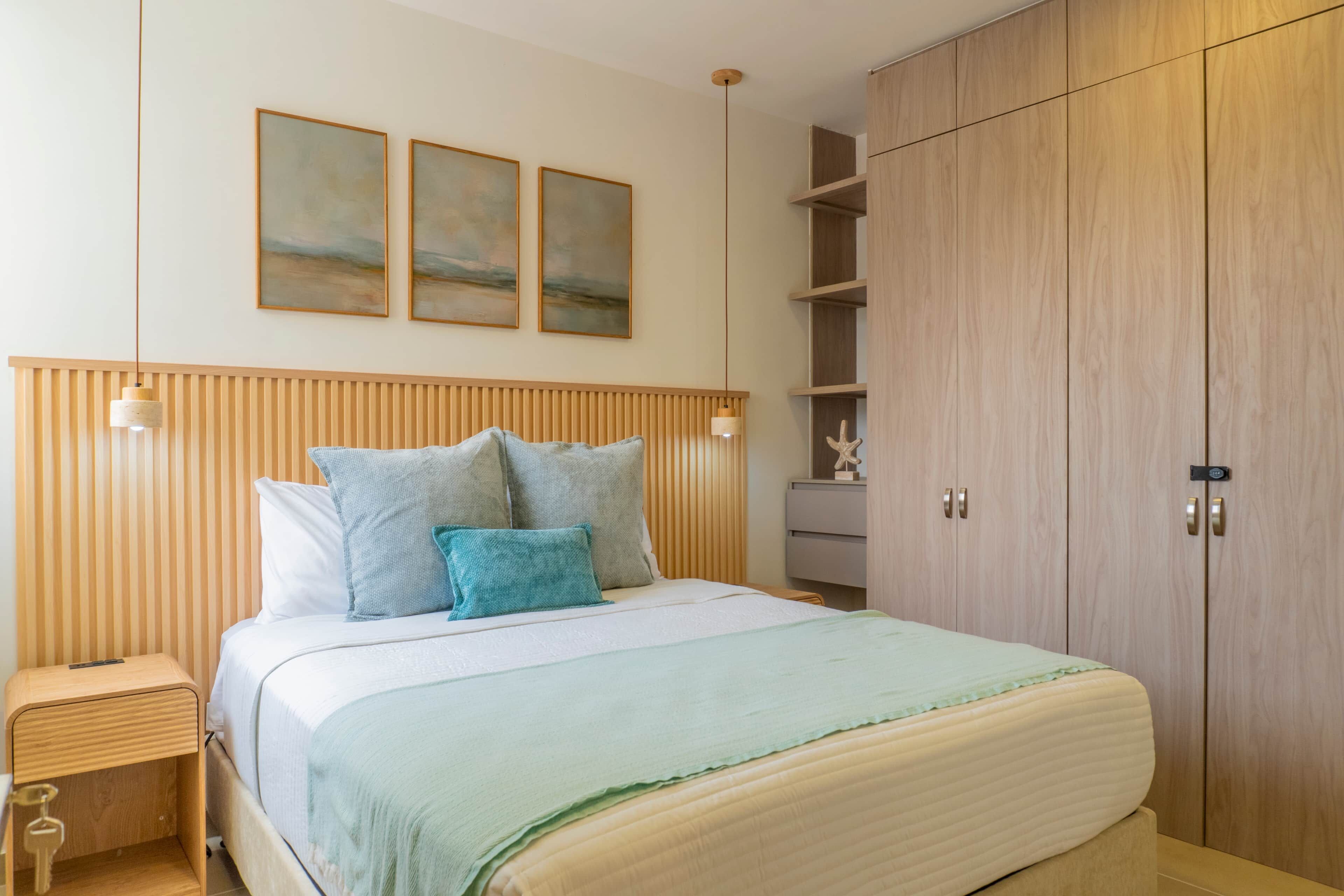 A bedroom with a bed, wooden headboard, bedside tables, a wardrobe, and wall-mounted artwork.