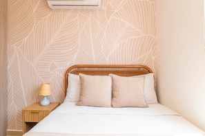 A bed with a headboard, two pillows, a bedside table with a lamp, and a wall with a leaf pattern. - Sereno Stays · 3BR Apartment, Santa Marta (Unknown)
