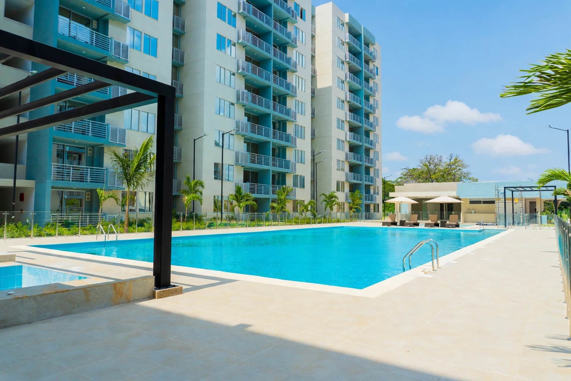 A modern hotel with a large swimming pool, outdoor seating, and a multi-story building with balconies.