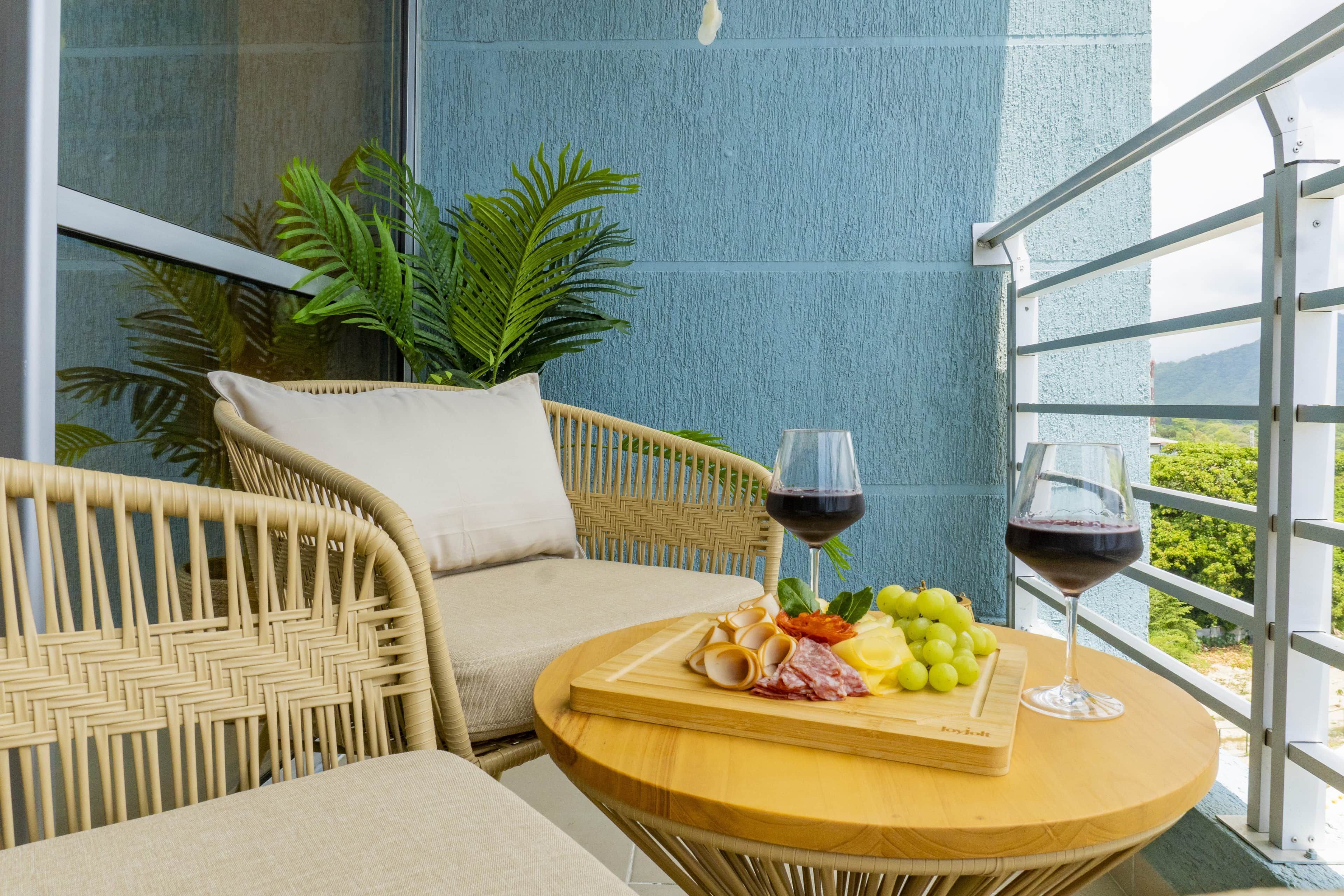 Une chaise en osier avec un coussin, une petite table ronde en bois avec une planche à découper et deux verres de vin rouge.