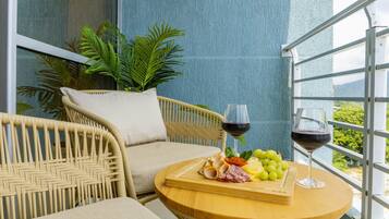 Une chaise en osier avec un coussin, une petite table ronde en bois avec une planche à découper et deux verres de vin rouge.