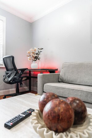 A living room with a grey sofa, a black office chair, a vase with flowers, and a remote control on a table. - Modern Apartment Near Union Market & NoMa (Washington)