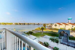 A river view from a balcony with a bridge in the background, a water tower, and a building with a red roof. - Palm Court Yacht Club 312a - Studio by the Sea (Fort Walton Beach)