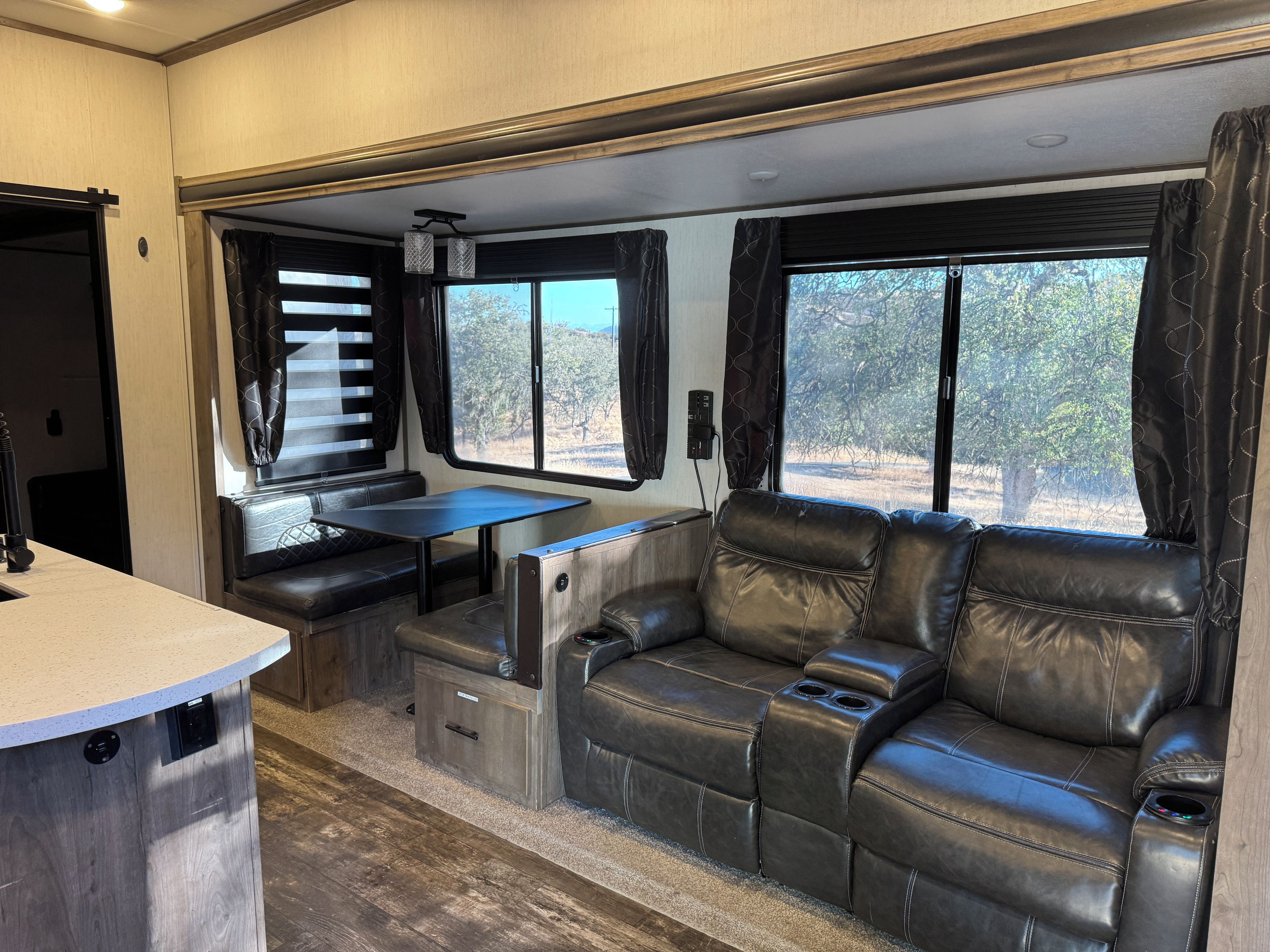 A compact RV interior with a kitchenette, seating area, and windows offering a view of the outdoors.