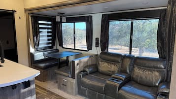 A compact RV interior with a kitchenette, seating area, and windows offering a view of the outdoors.