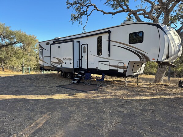 Una caravana Sabre Cobalt estacionada en un terreno seco y cubierto de hierba, con árboles al fondo.