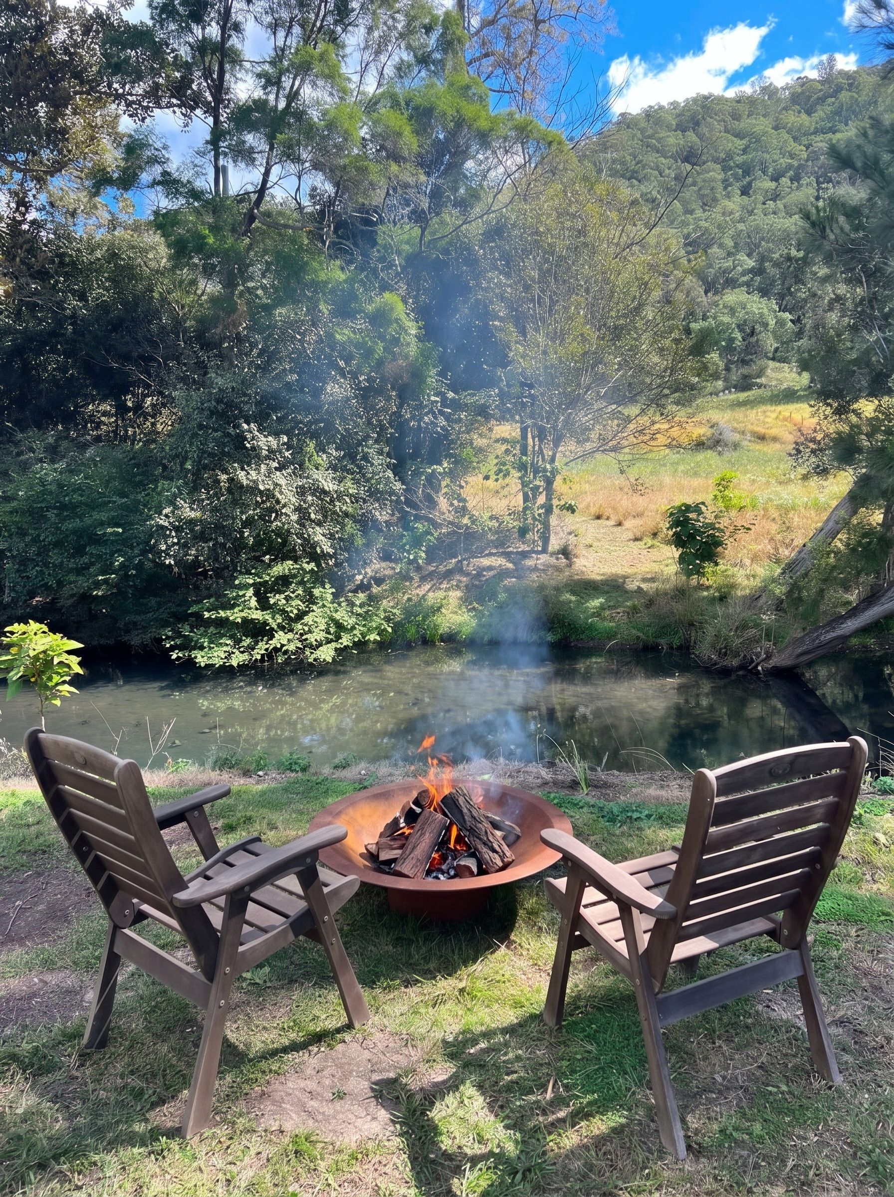 A campsite with a fire pit and two chairs by a river.