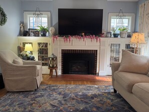 Una sala de estar con chimenea, dos sofás, un tapete estampado y un televisor sobre la chimenea.