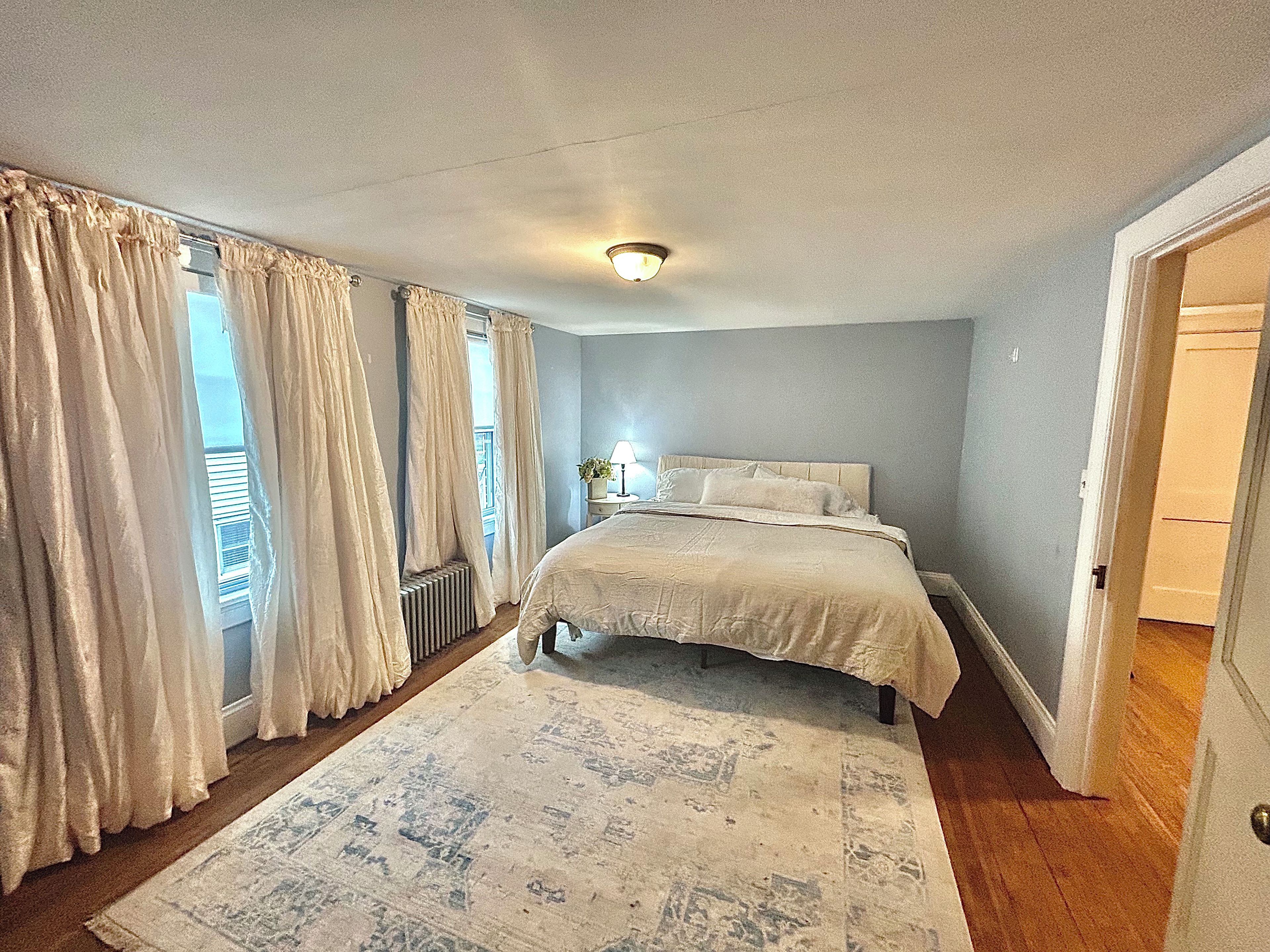 Un dormitorio con una cama grande, una mesita de noche, una ventana con cortinas y vistas al exterior.