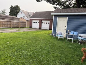 A residential backyard with a blue shed, a white garage, and a wooden fence. - Classic Cape with Modern Cottage Charm (Horseheads)