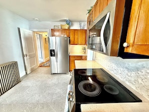 A kitchen with a stainless steel refrigerator, wooden cabinets, a black stove, and a tiled floor. - Classic Cape with Modern Cottage Charm (Horseheads)