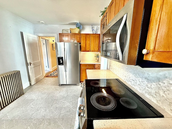 A kitchen with a stainless steel refrigerator, wooden cabinets, a black stove, and a tiled floor. - Classic Cape with Modern Cottage Charm (Horseheads)