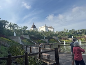 Ein Park mit einer schlossartigen Struktur, einer Holzbrücke und einem Brunnen.