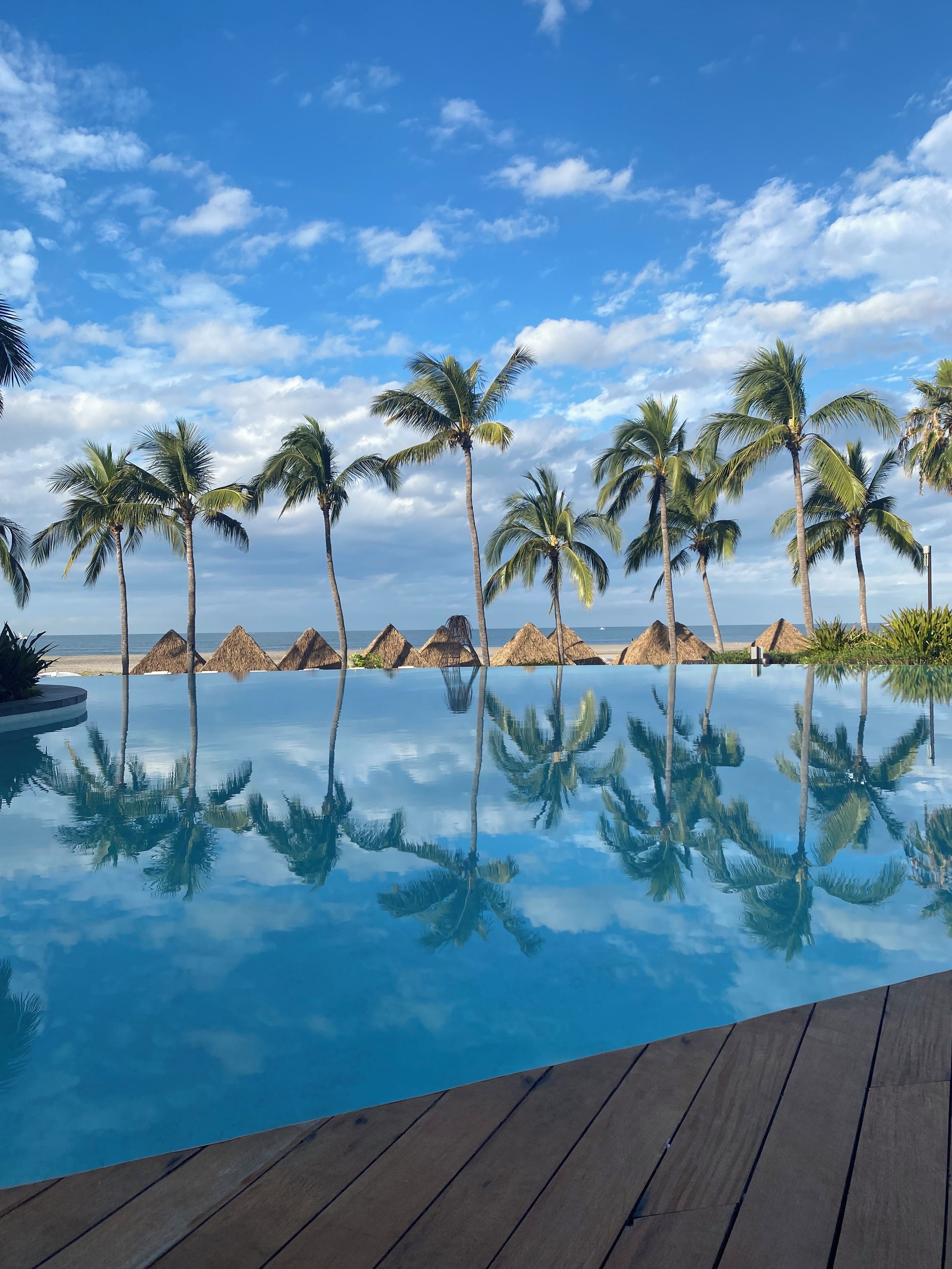 A clear blue pool with reflections of palm trees and a wooden deck.