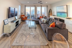 A modern living room with a sofa, coffee table, and TV. There is a balcony with a view. - NEW Rooftop Retreat |Ocean, Marina Views |Elevator (Carolina Beach)