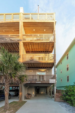 A multi-story building with a wooden facade, a covered outdoor area, and a sign indicating 'HOST HELP' services. - NEW Rooftop Retreat |Ocean, Marina Views |Elevator (Carolina Beach)
