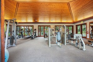 Ein Fitnessstudio mit verschiedenen Trainingsgeräten, großen Fenstern und einer Holzbalkendecke.