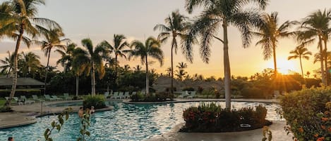 A swimming pool with palm trees and a sunset in the background.