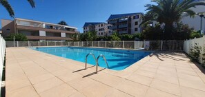 A swimming pool with two ladders, surrounded by a white fence, with buildings in the background. - T2 in Lavandou - Residence with Swimming Pool (Le Lavandou)