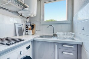 A compact kitchen with a built-in stove, a sink, and a window providing natural light. - T2 in Lavandou - Residence with Swimming Pool (Le Lavandou)
