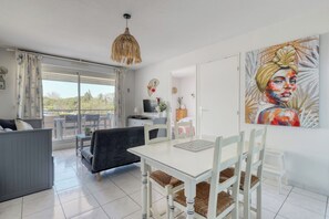 A modern living room with a dining area, large windows, and a painting on the wall. - T2 in Lavandou - Residence with Swimming Pool (Le Lavandou)