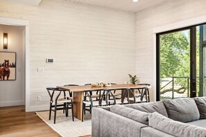 A modern interior with a dining area, a sofa, and a large window. - Luxe 3BR Lake Stay | BBQ | Firepit | Pickleball (Spicewood)